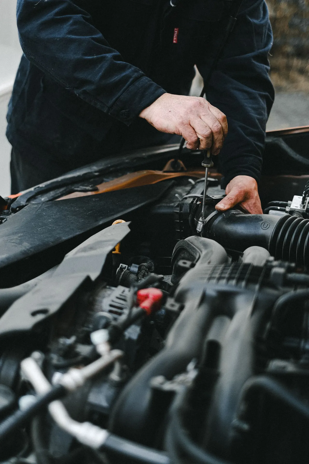 Mechanic working on a car engine intake with a hand tool.